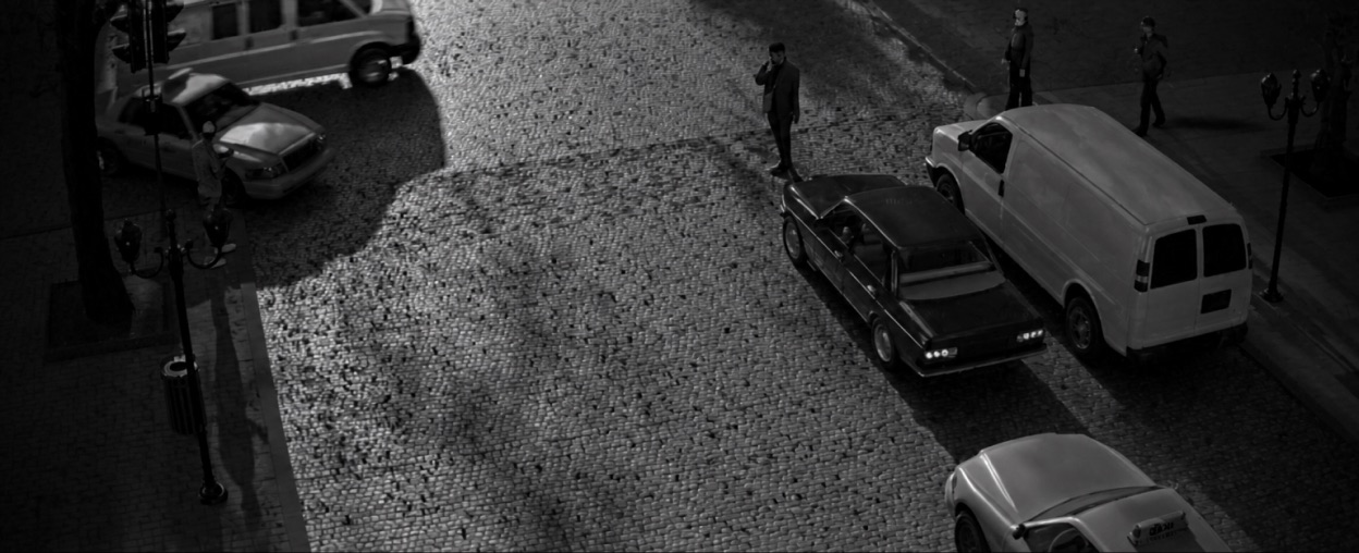 Night-time street camera view of a parked van and figures on the pavement.